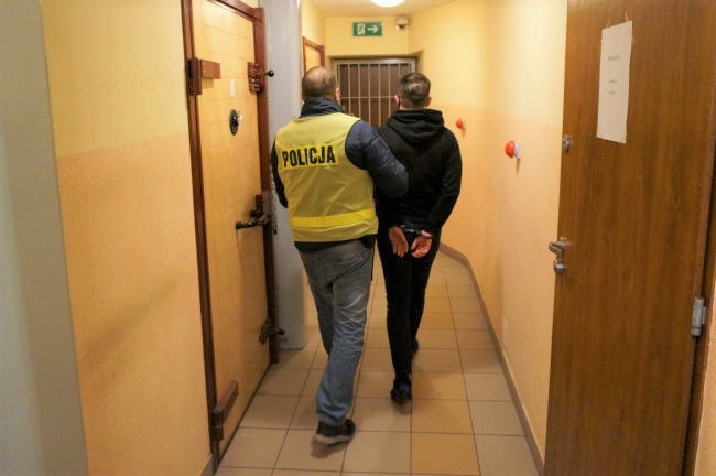 Policjant prowadzi zatrzymanego korytarzem aresztu