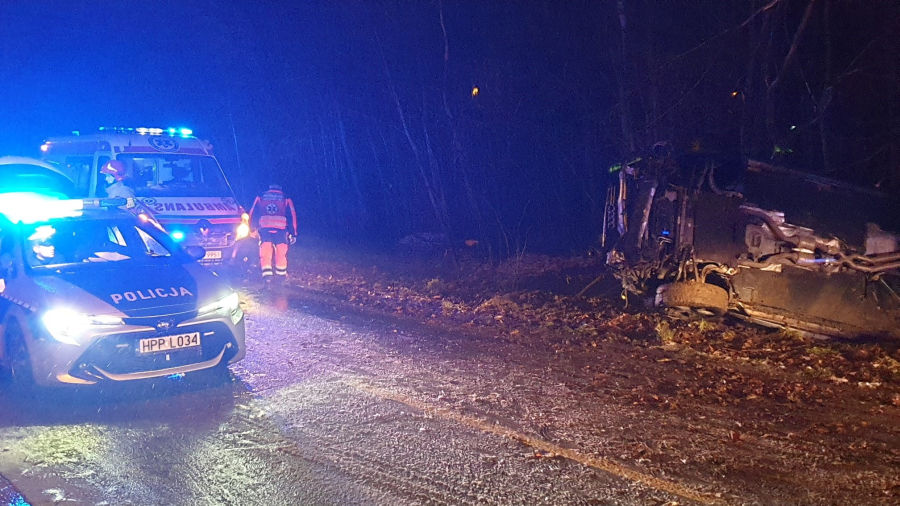 Na zdjęciu miejsce kolizji, widoczne samochody służb i pojazd na boku.