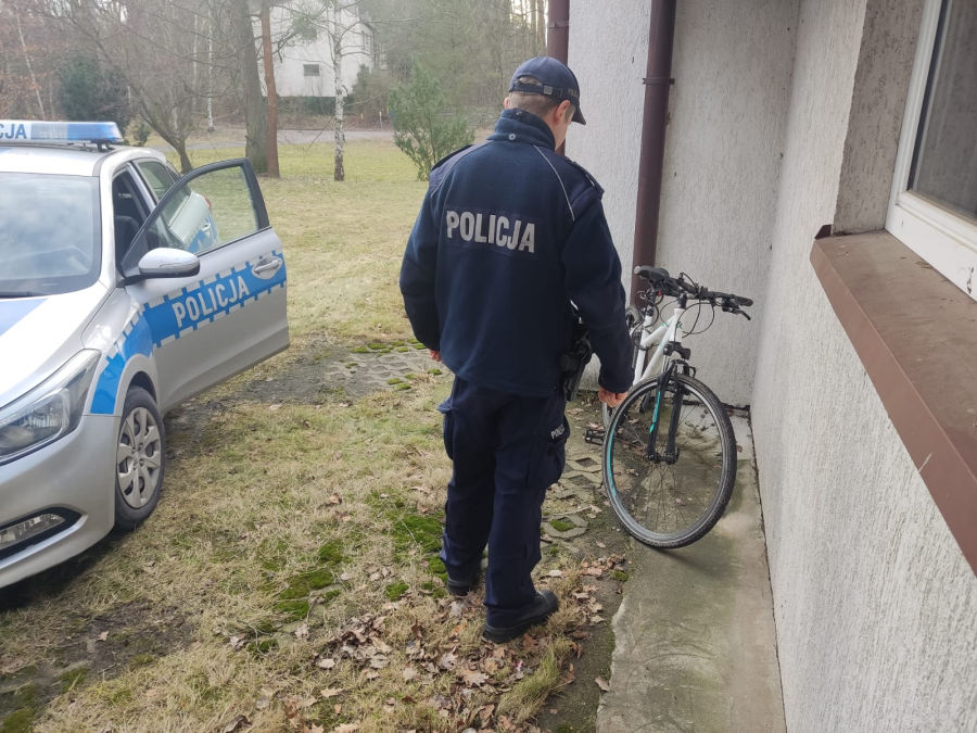 Na zdjęciu policjant stojący obok roweru, obok policyjny radiowóz. 