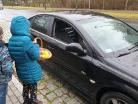 Na zdjęciu dziewczynka z koszem owoców stoi koło czarnego pojazdu w czasie akcji profilaktycznej.