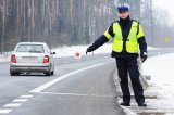 Na zdjęciu policjant stojący przy drodze zatrzymuje pojazdy tarcza do zatrzymywania pojazdów.