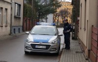 Na zdjęciu policjant w mundurze stojący obok radiowozu.