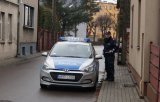 Na zdjęciu policjant w mundurze stojący obok radiowozu.