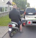 Na zdjęciu widoczny zatrzymany nietrzeźwy kierujący motorowerem a przed min stojący pojazd koloru czarnego.