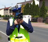 Na zdjęciu policjant wydziału ruchu drogowego z urządzeniem do pomiaru prędkości pełniący służbę na drodze.