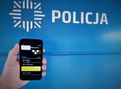 Na zdjęciu widoczny telefon komórkowy z uruchomioną aplikacja mobilną oraz logo i napis Policja.