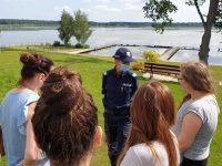 Na zdjęciu widoczna policjantka w mundurze, przed nią stoją osoby rozmawiające  i zadające pytania.