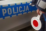 Na zdjęciu policyjna tarcza do zatrzymywania pojazdów trzymana w ręce przez policjanta oraz widoczny napis Policja na drzwiach radiwowozu.