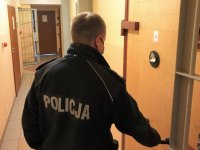 Na zdjęciu policjant w mundurze otwiera drzwi więziennej celi.