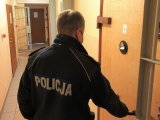 Na zdjęciu policjant w mundurze otwiera drzwi więziennej celi.