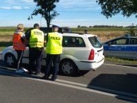 Na zdjęciu policjant , funkcjonariusz SOK i pracownica PLK rozmawiają z kierowcą białego auta oczekującego na otwarcie przejazdu kolejowego.