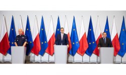 Na zdjęciu kadr z konferencji prasowej ,stojący za mównicą na tle flag polskich i Unii Europejskiej Premier Mateusz Morawiecki w środku, po prawej Minister MSWiA Mariusz Kamiński , po lewej Komendant Główny Policji gen. insp. Jarosław Szymczyk.