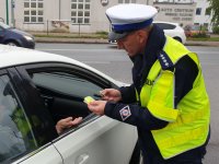 Na zdjęciu policjant stojący przy samochodzie wręcza odblaski w czasie Dnia Odblasków.