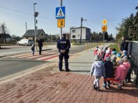 Na zdjęciu funkcjonariusze Policji wraz z przedszkolakami stojący w rejonie przejścia dla pieszych.