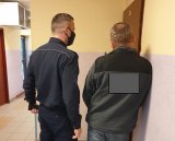 Na zdjęciu policjant i zatrzymany mężczyzna stojący przed drzwiami do policyjnego aresztu.