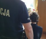 Na zdjęciu policjant stojący za mężczyzną siedzącym na krześle.