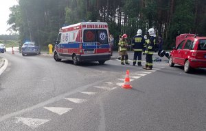 Na zdjęciu miejsce wypadku w Koszęcinie, widoczny rozbity pojazd osobowy i leżący motoicykl, a także pojazdy służb.