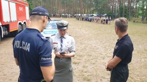 Na zdjęciu policjant w trakcie kontroli obozu harcerskiego w Kokotku rozmawia z kobietą w mundurze harcerskim.