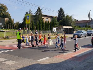 Na zdjęciu uczniowie w asyście policjntów przechodzą przez przejście dla pieszych koło szkoły w Sadowie.