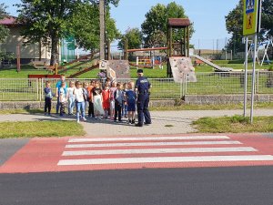 Na zdjęciu uczniowie i policjantka stoją przed przejściem dla pieszych koło szkoły w Sadowie.