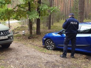 Na zdjęciu policjant kontrolujący pojazd w obszarze leśnym.