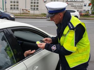 Na zdjęciu policjant wręcza odblaski pasażerowi zatrzymanego pojazdu.