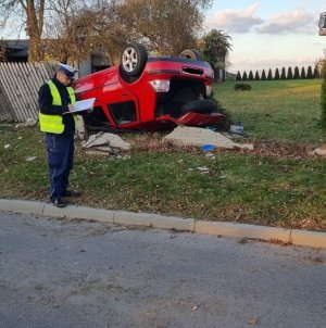 Na zdjęciu policjant w trakcie czynności w Babienicy, w tle rozbity samochód osobowy.