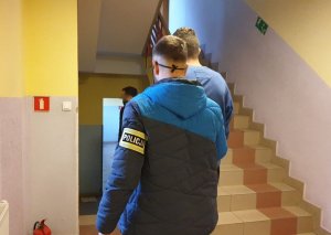 Na zdjęciu policjanci kryminalni prowadzą zatrzymanego mężczyznę po schodach w komendzie w Lublińcu.