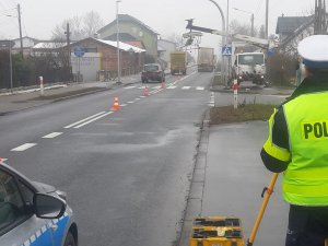 Na zdjęciu policjant ruchu drogowego wykonuje czynności w miejscu poważnego wypadku drogowego na krajowej 11-stce w miejscowości Glinica. W tle przejeżdżają pojazdy.