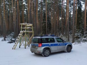 Na zdjęciu policyjny radiowóz stojący na tle ambony myśliwskiej.