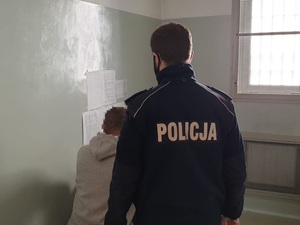 Na zdjęciu widok policyjnej celi i policjant pilnujący zatrzymanego mężczyny.