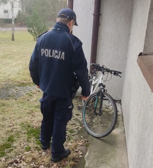 Na zdjęciu policjant w mundurze stojący obok roweru.