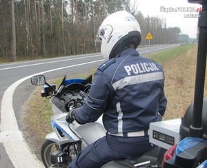 Na zdjęciu policjant pełniący służbę na motocyklu obserwuje drogę.