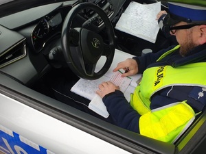 Na zdjęciu policjanci siedzący w radiowozie wypisują mandat karny.