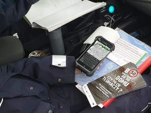 Na zdjęciu wnętrze radiowozu, widoczne urządzenie elektroniczne do weryfikacji danych kierowcy i ulotki profilaktyczne.