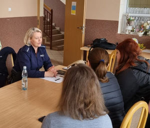 Na zdjęciu policjantka siedząca przy stole w trakcie spotkania profilaktycznego z uchodźcami z Ukrainy w jednym z ośrodków na terenie powiatu lublinieckiego.