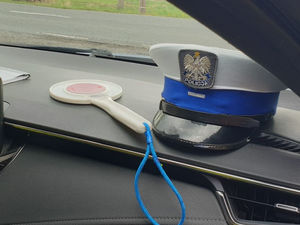 Na zdjęciu policyjna czapka i tarcza do zatrzymywania pojazdów leżące na podszybiu radiowozu.