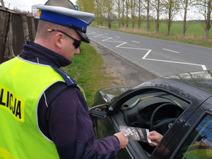 Na zdjęciu policjant wręcza kierującemu ulotkę profilaktyczną.