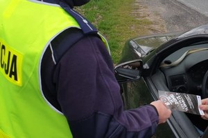 Na zdjęciu policjant wręcza kierowcy ulotkę profilktyczną.