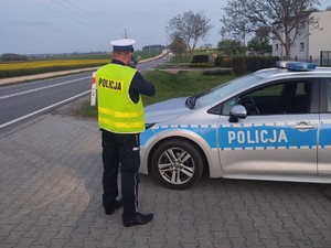 Na zdjęciu policjant drogówki w trakcie pełnienia służby na drodze. policjant stoi obok radiowozu.