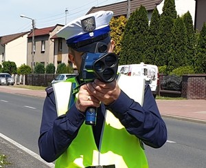 Na zdjęciu policjant dokonujący pomiaru prędkości na drodze.