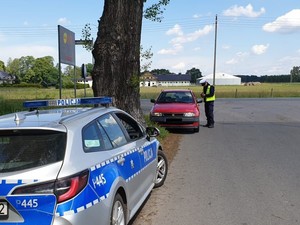 Na zdjęciu policjant w trakcie kontroli samochodu na drodze.