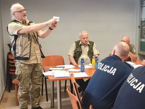 Na zdjęciu uczestnicy szkolenia w lublinieckiej Komendzie Policji siedzący przy stole. Funkcjonariusz Straży Rybackiej demonstruje dokumenty wymagane w czasie kontroli osoby poławiającej ryby.