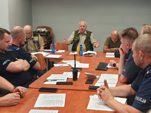Na zdjęciu uczestnicy szkolenia w lublinieckiej Komendzie Policji siedzący przy stole. Na drugim planie widoczni funkcjonariusze Straży Rybackiej.