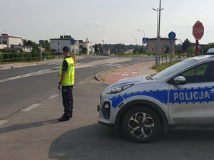 Na zdjęciu policjant zabezpieczający trasę wyścigu stojący obok radiowozu.