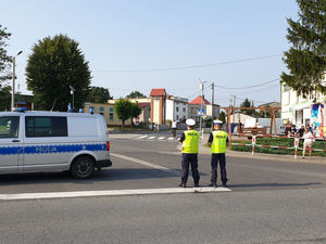 Na zdjęciu dwóch policjantów  w trakcie zabezpieczenia trasy wyścigu kolarskiego w Woźnikach kierujących ruchem na drodze.