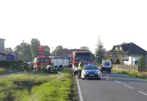 Na zdjęciu miejsce wypadku w Gwoździanach, na poboczy widoczny rozbity pojazd, policyjny radiowóz i wozy strażackie.