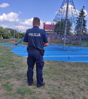 Zdjęcie przedstawia policjanta, w tle widać urządzenia przeznaczone dla rozrywki dla młodzieży.