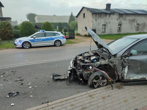 Na zdjęciu widoczny rozbity samochód biorący udział w kolizji w Sadowie, a w tle policyjny radiowóz.