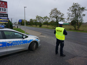 Na zdjęciu policjant stojący na drodze obok radiowozu.